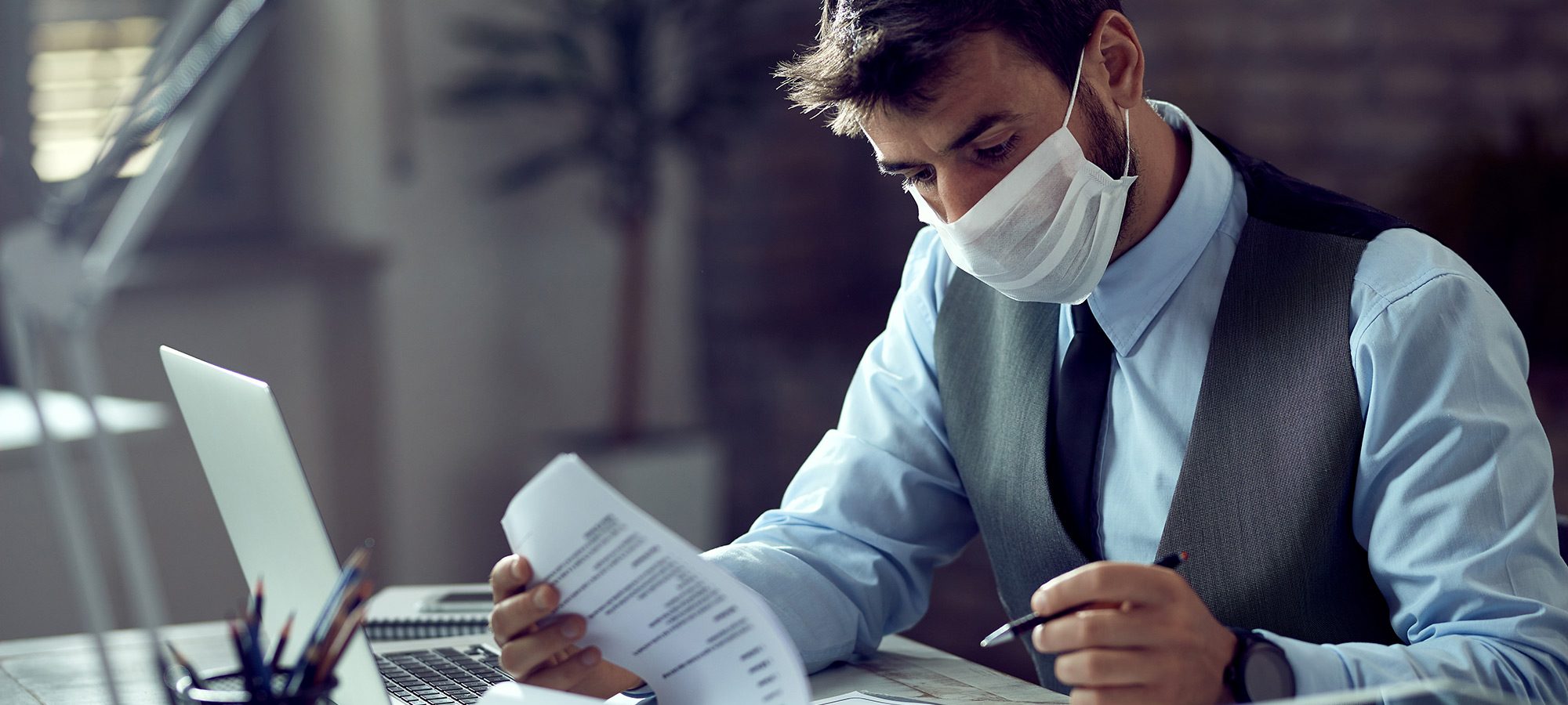 male-entrepreneur-analyzing-business-reports-while-wearing-face-mask-working-office-virus-epidemic